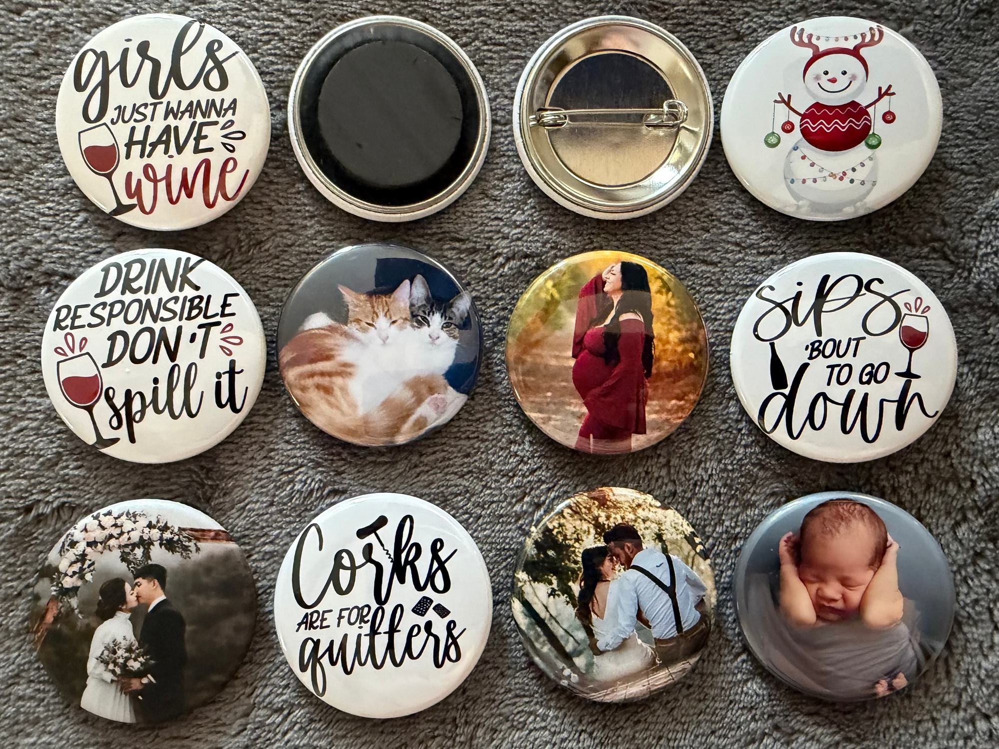 Collection of various 1.5 inch round pin buttons and magnets with different designs.  The buttons and magnets are photographed against a soft gray surface background.