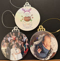 Three samples of Holiday/Christmas ornaments featuring a snowman and two babies on a dark surface.  Gold or silver colored wooden ornament backing with a gold or silver string to hang the ornament.  One ornament has a clear covering, while the other  have clear holographic covering.