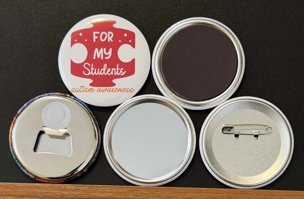 A white round button with a red puzzle piece with 'For my Students' in white text and 'autism awareness' orange text on a white background.  the other 4 buttons show the backside options which include magnet magnetic bottle cap opener, pin back button and pocket mirror.  Photographed on a black background.