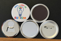 A white round button with 'Shine a light on autism' in multi-colored text, with a blue light bulb containing a multi-colored puzzle piece puzzle  on a white background.  The other 4 buttons show the backside options which include magnet magnetic bottle cap opener, pin back button and pocket mirror.  Photographed on a black background.