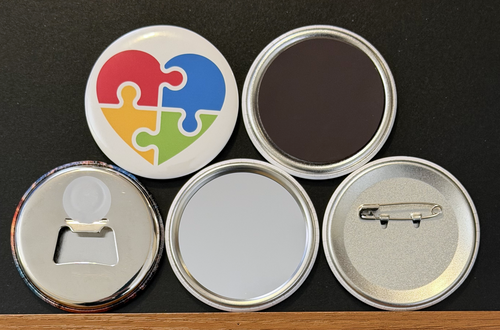 A white round button with a multi-colored puzzle piece heart on a white background.  The other 4 buttons show the backside options which include magnet magnetic bottle cap opener, pin back button and pocket mirror.  Photographed on a black background.