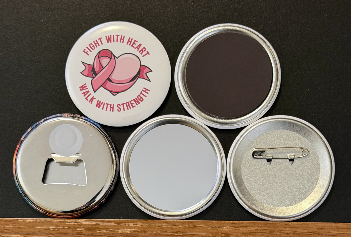 Round white magnet with the message 'Fight with heart, walk with strength'' in pink text with a pink breast cancer ribbon wrapped around a pink heart.  Also in the photo are the four options available for this magnet which include a pin back button, pocket mirror, magnetic bottle opener and magnet.  This image was photographed on a black background.