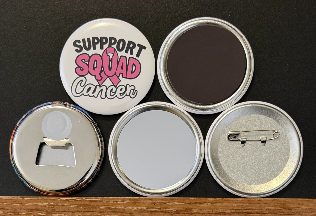Round white magnet with the message 'Support Squad Cancer' in black and pink text with a pink breast cancer ribbon.  Also in the photo are the four options available for this magnet which include a pin back button, pocket mirror, magnetic bottle opener and magnet.  This image was photographed on a black background.