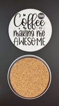 Round white drink coaster with cork backing with 'Coffee is making me awesome' in black text, with little black hearts, stars and coffee beans, photographed on a black background.