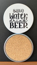 White round drink coaster with a cork backing with a black image of a beer glass with text 'save water, drink beer' on a white background.  This photo was taken on a black background.