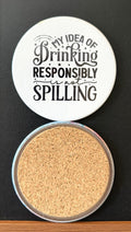 White round drink coaster with a cork backing with black decorative accents with text 'my idea of drinking responsibly is not spilling' on a white background.  This photo was taken on a black background.