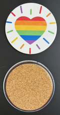 White round drink coaster with a radiating rainbow heart image, with a cork backing  This photo was taken on a black background.