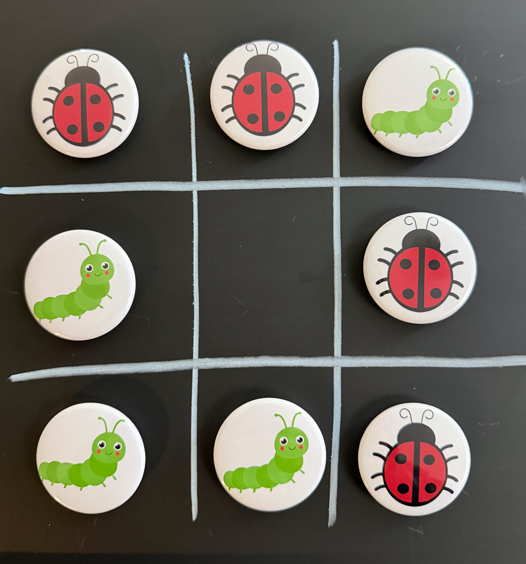 8 Tic Tac Toe small round magnets on a black background with a white grid pattern.  4 game pieces have  red and black lady bug images and the other 4 images are green caterpillars with a smiling face.  