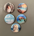 Set of five round magnets with beach-themed images photographed against a gray surface