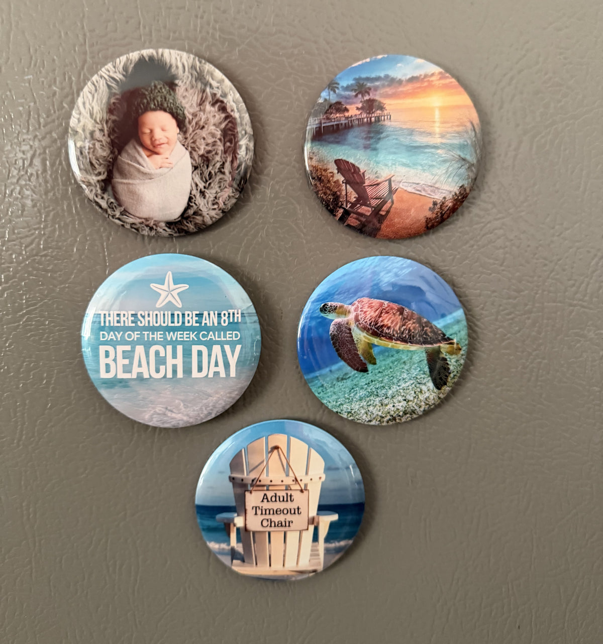 Set of five round magnets with beach-themed images photographed against a gray surface