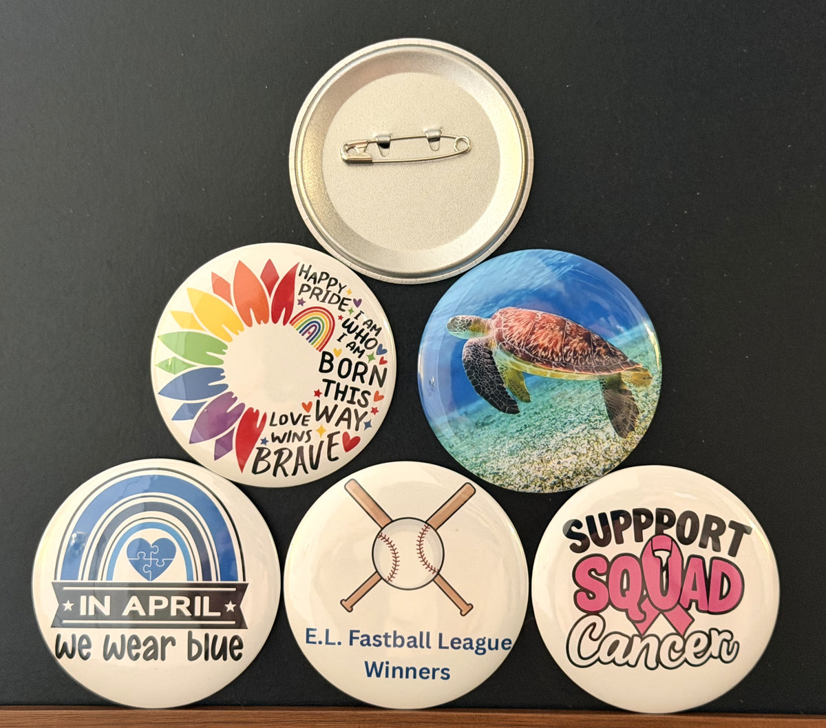 A collection of round images buttons with one being the back showing the pin clasp, photographed on a dark background. 
