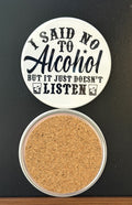 Round white drink coaster with cork backing with 'I said no to alcohol but it just doesn't listen' in black text, with two drink glasses with ice and liquor, photographed on a black background.