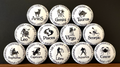 Set of white round magnets/buttons with black text each of the 12 zodiac signs with each button displaying different characteristics associated with each zodiac sign, arranged in a pyramid formation on a dark background.