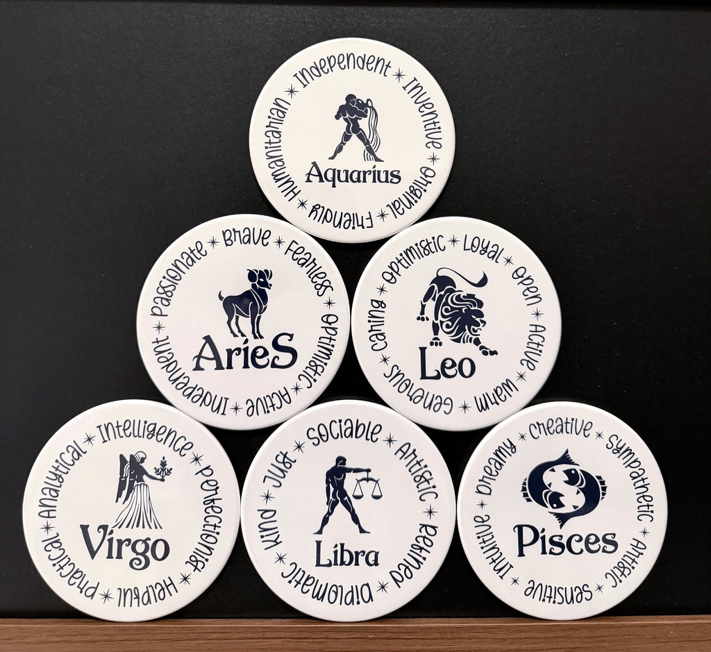 Set of 6 white zodiac drink coasters with dark navy blue text each of the 6 of 12 zodiac signs with each button displaying different characteristics associated with each zodiac sign, arranged in a pyramid formation on a dark background.