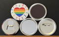 Round white magnet with a radiating rainbow colored heart image.  Also in the photo are the four options available for this magnet which include a pin back button, pocket mirror, magnetic bottle opener and magnet.  This photo was photographed on a black background.