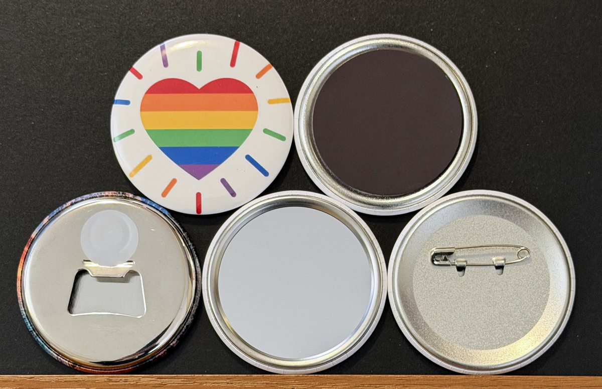 Round white magnet with a radiating rainbow colored heart image.  Also in the photo are the four options available for this magnet which include a pin back button, pocket mirror, magnetic bottle opener and magnet.  This photo was photographed on a black background.