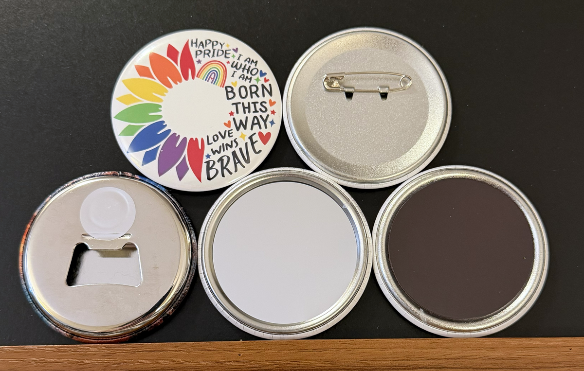 Round white magnet with a half image of a rainbow colored flower/petals with various pride-relates messages on the other side in black text with small multi-colored hearts and stars.  Also in the photo are the four options available for this magnet which include a pin back button, pocket mirror, magnetic bottle opener and magnet.  This photo was photographed on a black background.