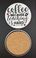 Round white drink coaster with cork backing with 'Coffee because teaching is hard' in black text, with small images of red apples, coffee beans and a coffee cup, photographed on a black background.