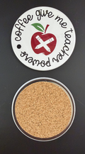 Round white drink coaster with cork backing with 'Coffee gives me teacher powers' in black text, with an image of an apple with two white pencils cross cross on the apple design, photographed on a black background.