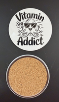 White round drink coaster with a cork backing with a black image of a smiling octopus wearing sunglasses with text 'vitamin sea addict' on a white background.  This photo was taken on a black background.