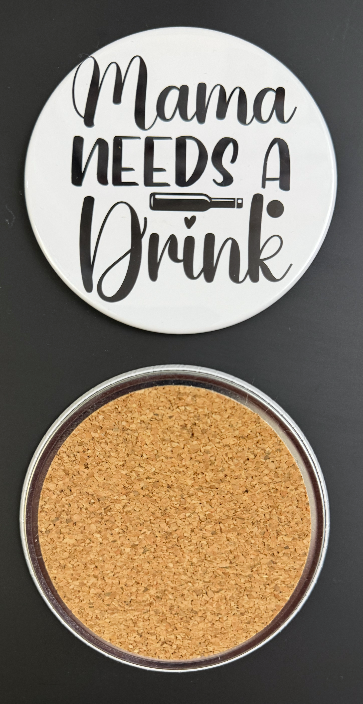 Round white drink coaster with cork backing with 'Mama Needs a Drink' in text black text, photographed on a black background.