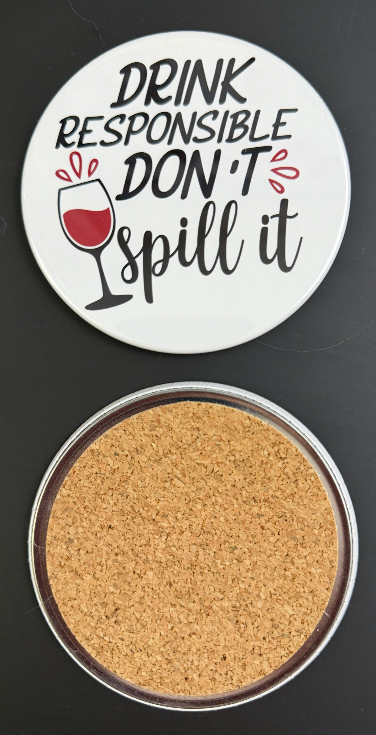 Round white drink coaster with cork backing with 'Drink Responsible Don't Spill It' in black text and a wine glass of red wine graphic on a black background.