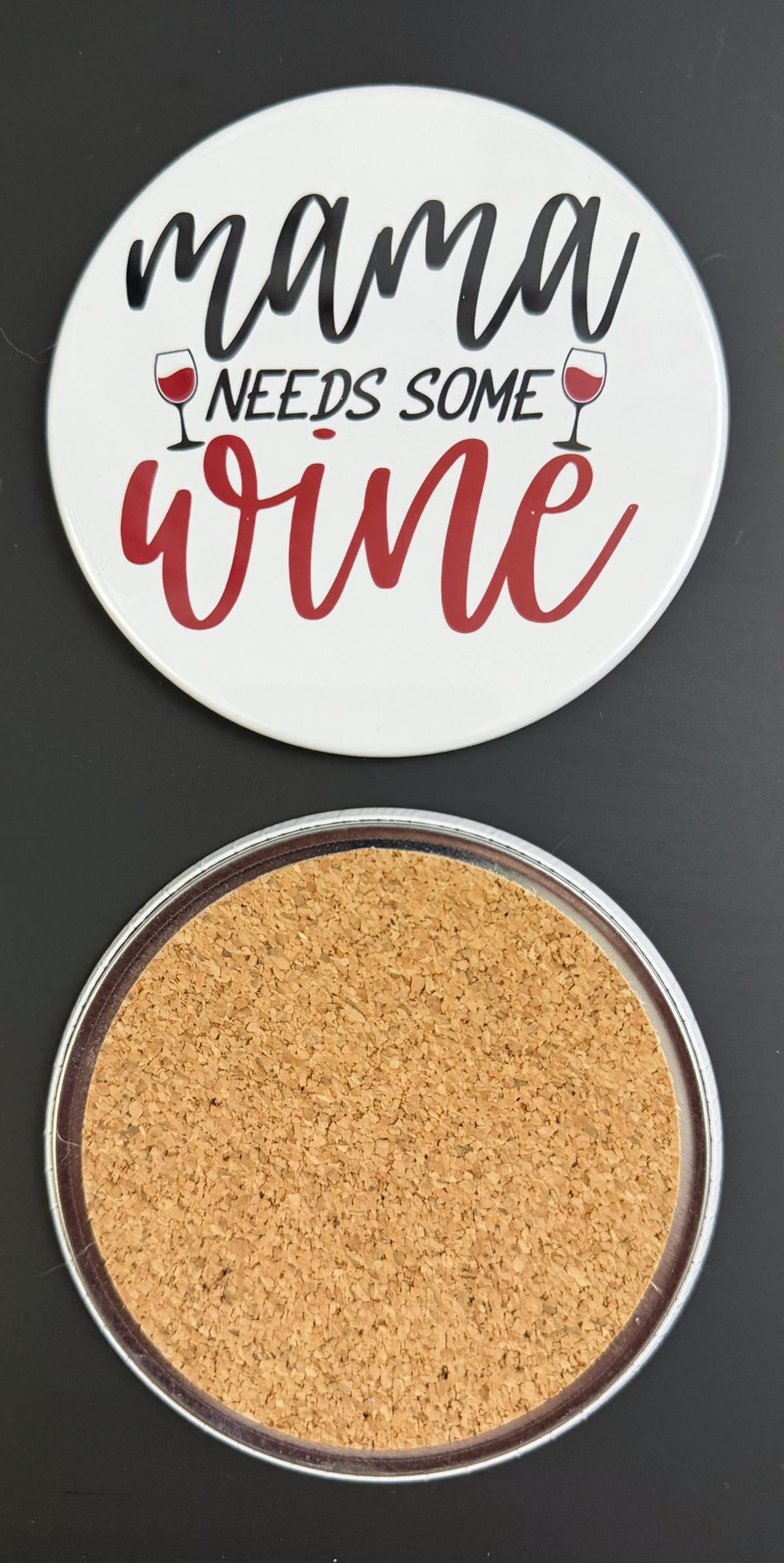 Round white drink coaster with cork backing with 'Mama Needs some wine' in red and black text, photographed on a black background.