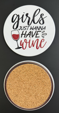 Round white drink coaster with cork backing with 'Girls just wanna have wine?' in red & black text with a glass of red wine, photographed on a black background.