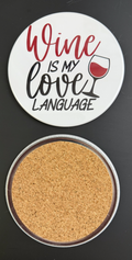 Round white drink coaster with cork backing with 'Wine is my love language' in red and black text, with a glass of red wine, photographed on a black background.