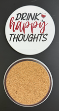 Round white drink coaster with cork backing with 'Drink Happy Thoughts' in red and black text, with a glass of red wine, photographed on a black background.