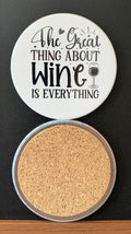 White round drink coaster with a cork backing with a black image of a black wine glass and black heart with text 'The great thing about wine is everything' on a white background.  This photo was taken on a black background.