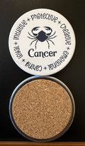Round white drink coaster with cork backing representing the Cancer zodiac design displaying different characteristics in dark navy blue text associated with the Cancer zodiac sign, on a black background.