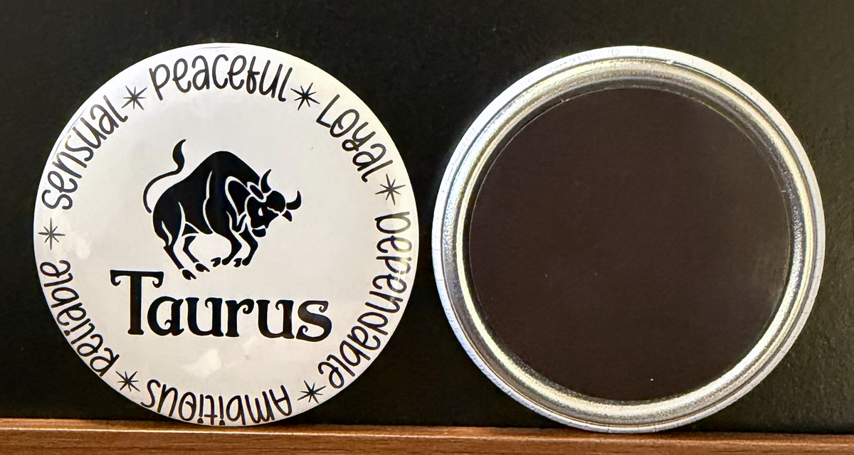 Round white magnet/button with black text for the Taurus zodiac sign  with black bull illustration on a white background, with characteristics for each zodiac sign in black text.